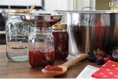 three various sized jam jars filled with jam, alongside a wooden spoon with a scooped portion of jam  